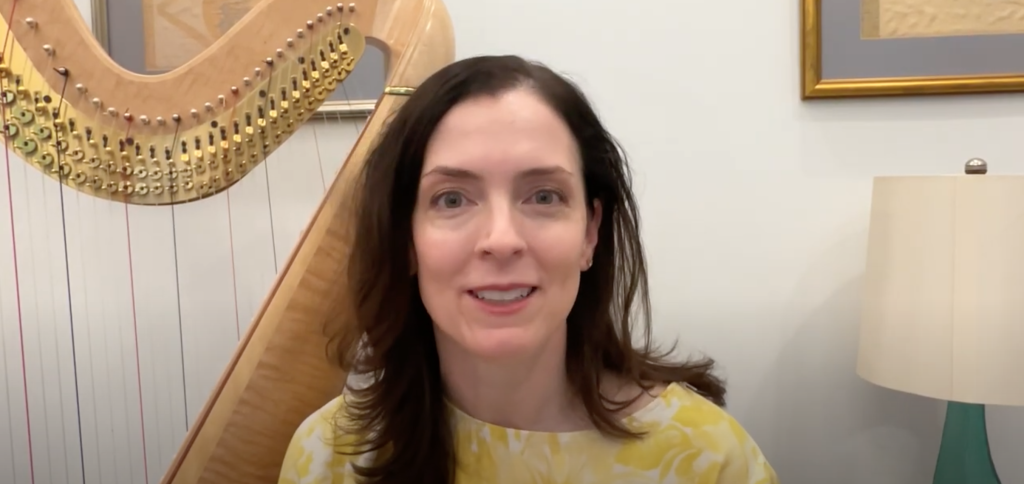 Video still of Elisabeth Remy Johnson next to a harp.